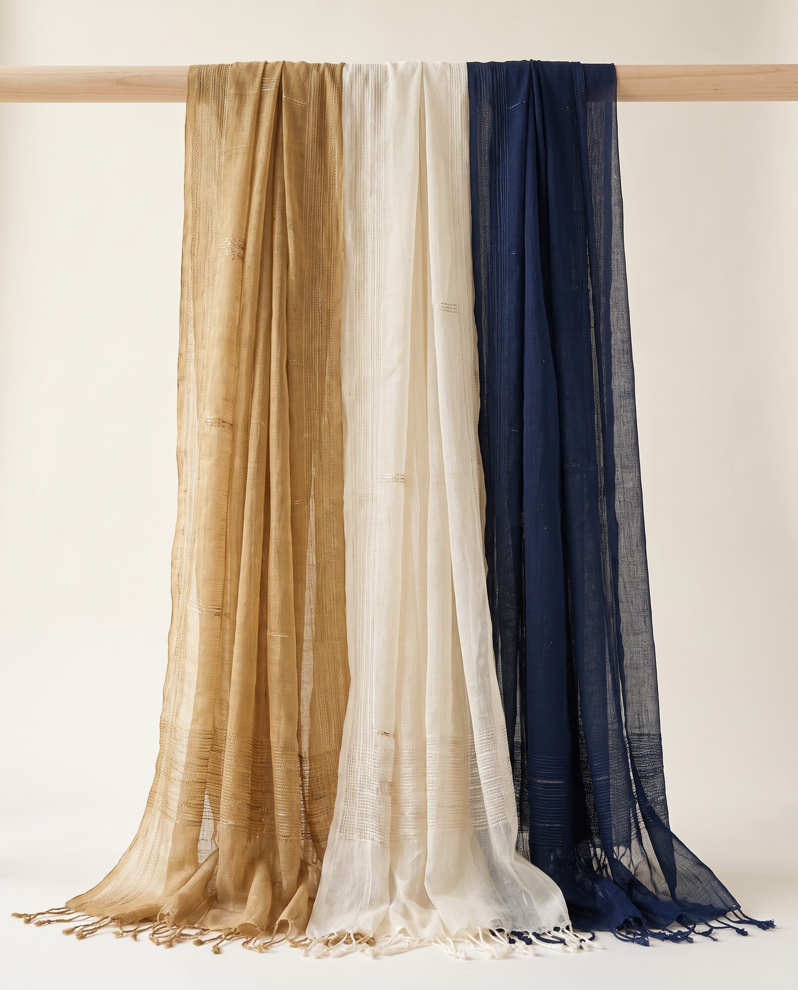 Silk and chiffon dupattas draped over a wooden rail in gold, ivory and navy